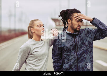 Diverse young couple in sportswear preparing for a run together outdoors on an overcast day Stock Photo