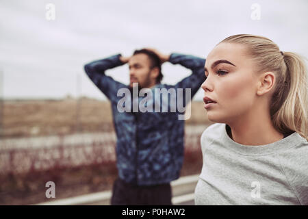 Diverse young couple in sportswear catching their breath while taking a break from a run together on an overcast day Stock Photo