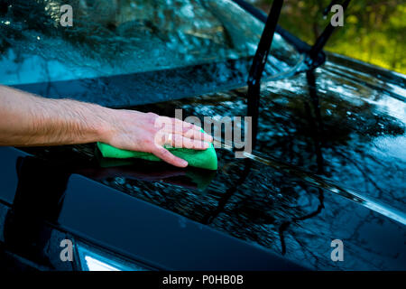 A man washes the car with a sponge and pours water on it with a hose. Close-up.cleaning automobile with sponge at car wash.Car washing concept. Copy space Stock Photo