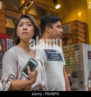 Standing together, looking away. Attractive young couple, asian woman, western man,   white shirts, brown skin, black hair. On the street, Shinjuku, T Stock Photo