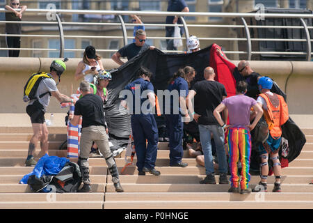 Daredevil basejumper seriously injured in Blackpool, Lancashire, UK. June 2018.  People rush to the aid of an injured base jumper who has crashed into the seaside promenade after a 400ft jump from a hired crane. A change in wind direction resulted in the canopy not fully opening which caused him to drift off course. Airgamez UK Base Jumping Championship event. Stock Photo