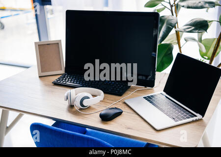 closeup view of workplace with laptop, headphones, photo frame and computer at table Stock Photo
