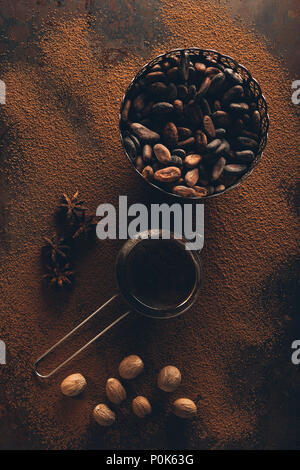 top view of gourmet cocoa beans in vintage bowl, sieve and star anise on cocoa powder Stock Photo