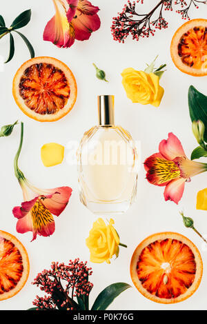 top view of bottle of aromatic perfume surrounded with flowers and blood orange slices on white Stock Photo