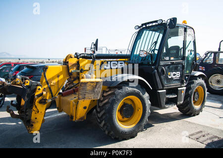 JCB digger in Lime Regis Uk England spade big large machine yellow  road works digging wheels large massive vehicle beach workers work sign signs Stock Photo