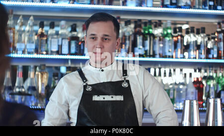 Cheerful young barman smiling and talking to client in bar Stock Photo