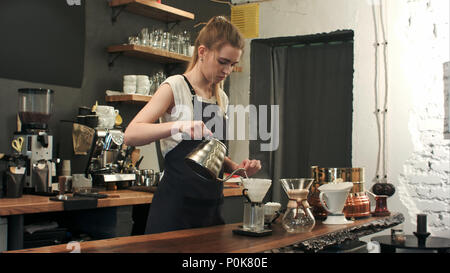 Young female barista in trendy modern cafe coffee shop pours boiling water over coffee grounds making a pour over drip coffee Stock Photo