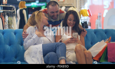 Beautiful young women with shopping bags and smartphone in mall meeting their male friend Stock Photo