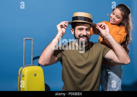 daughter putting straw hat on father on blue Stock Photo