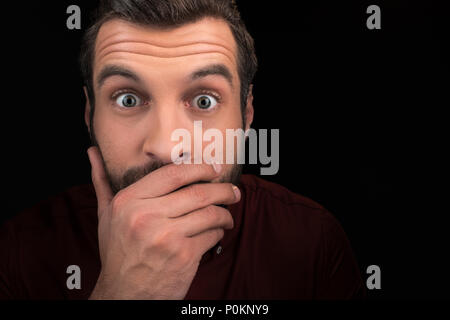 portrait of shocked man covering mouth isolated on black Stock Photo