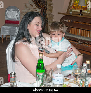 Close-up indoor portrait of smiling brunette woman that is comforting her child sitting at table. Stock Photo