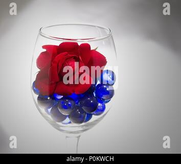 Red rose on a bed of blue gemstones in a wineglass Stock Photo