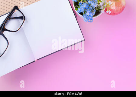 Glasses on an open notepad. Pink background and blue flowers . Flat lay. Copt space Stock Photo