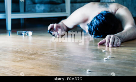 Mature man lying on the floor for overdose with pills calling for help using his mobile. Stock Photo