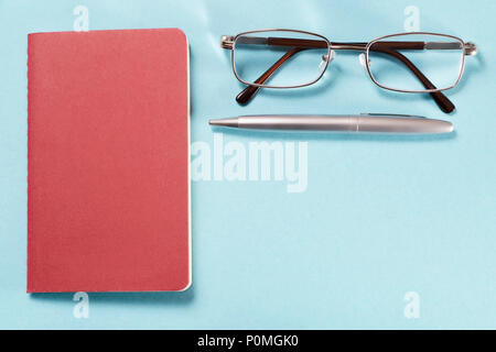 Glasses, pen and notebook. Top view on blue cardboard background with copy space. Template and background Stock Photo