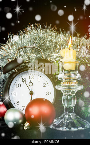 Beautiful Christmas card with clock, Christmas balls and a burning candle in a crystal candlestick against the background of fir branches and silvery  Stock Photo