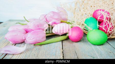 Easter composition with pink tulip flowers, painted Easter eggs and wicker basket are on the old blue wooden background Stock Photo