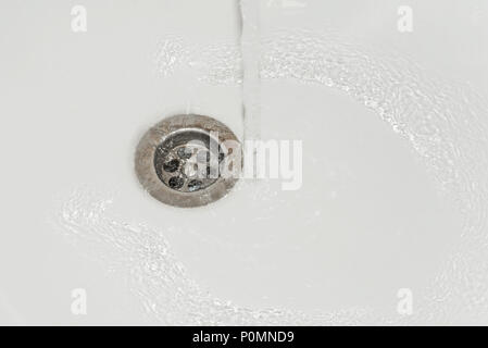 Stream of purified drinking water pours into the white faience sink and flows into the sewer Stock Photo