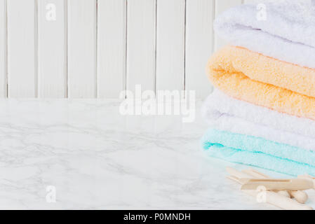 Stack of multicolored fluffy cotton bath towels and wooden clothespins are on the background of marble surface, with copy-space Stock Photo