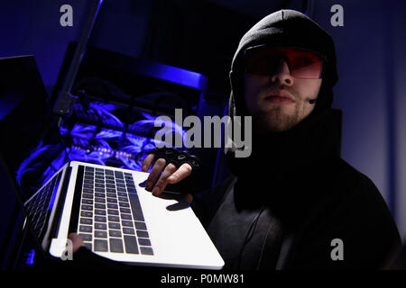 side view of hacker in eyeglasses with laptop looking away with cables on background Stock Photo