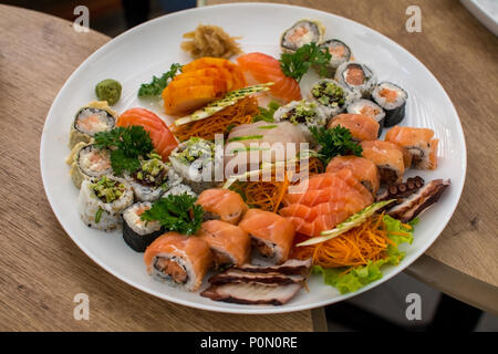 Sushi, sashimi and rolls plate in Japanese Restaurant setting, on white plate, between two round wooden tables- Asian food concept Stock Photo