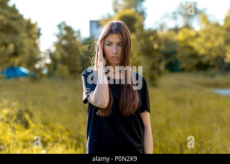 A brunette girl in the fresh air in a black T-shirt. He presses his hand with his temple. Emotions a headache. Migraines and bad thoughts. Stock Photo