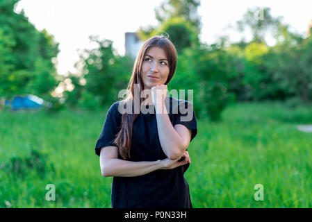 Beautiful brunette girl in summer in a park outdoors with a hands gesture showing a thoughtful look. Dreams of something more. She looks upwards at sky with her eyes. Long brown hair. Happy smiling. Stock Photo