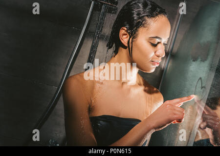 attractive african american woman taking shower and drawing heart sign on glass Stock Photo