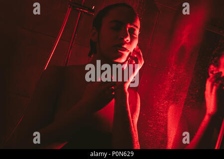 attractive african american woman taking shower, in red light Stock Photo