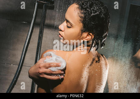 back view of attractive african american woman with sponge taking shower Stock Photo