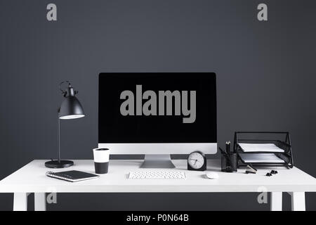 desktop computer with blank screen, clock and office supplies at workplace Stock Photo