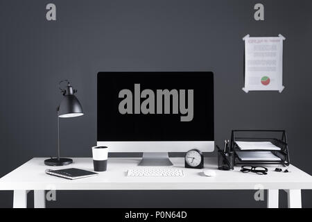 desktop computer with blank screen, business chart, clock and office supplies at workplace Stock Photo