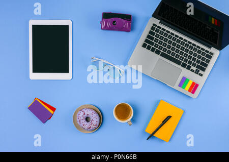 top view of laptop, digital tablet, cup of coffee with doughnut and camera on blue Stock Photo