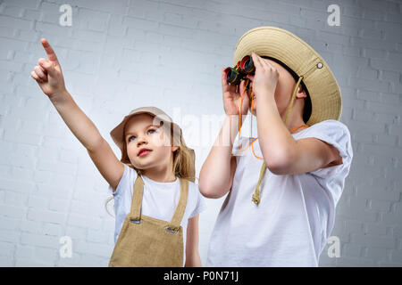 children in safari costumes and hats pointing and looking in binoculars Stock Photo