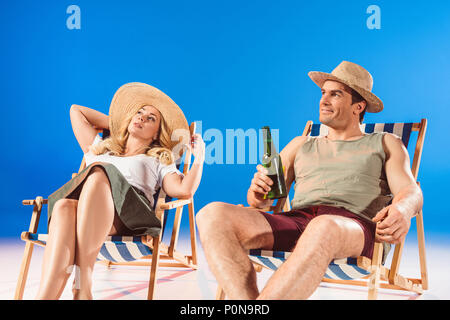 Woman sitting in lounge chair by man with beer on blue background Stock Photo