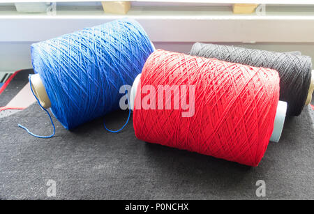 Three big white Bobbins with colored blue, black and red threads in the studio. Novosibirsk, Russia Stock Photo