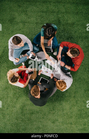 overhead view of businesswomen shaking hands while other colleagues having discussion on grass Stock Photo