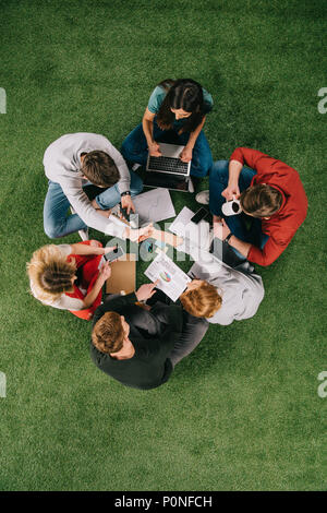 overhead view of two business colleagues shaking hands while other partners having discussion on grass Stock Photo