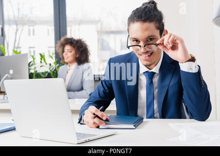 Young man in eyeglasses working on laptop by office table Stock Photo