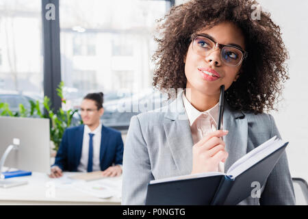 Dreamy girl holding notebook and thinking in modern office Stock Photo