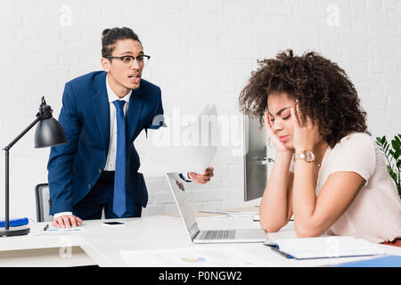 Businessman yelling at businesswoman by table in office Stock Photo