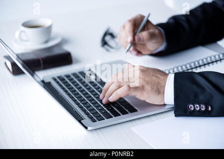 cropped view of businessman working with laptop and making notes Stock Photo