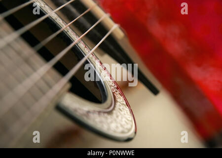 Detail on classical guitar six string, shallow depth of focus, with blurred red background. Stock Photo