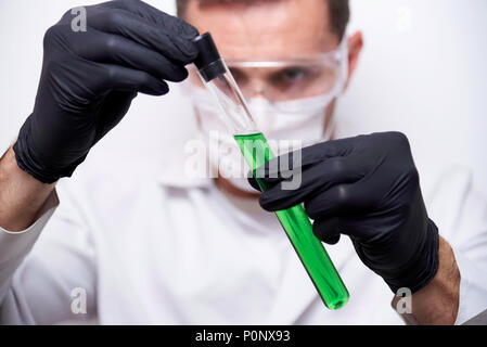 Hands of a scientist in black gloves holding a test tube with a dangerous green chemical liquid on a white background. Stock Photo
