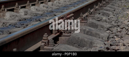 Selective field of focus. Detail of rusty screws and nut on old railroad track. Concrete tie with rusty nuts and bolts. Damaged surface of rail rod. N Stock Photo