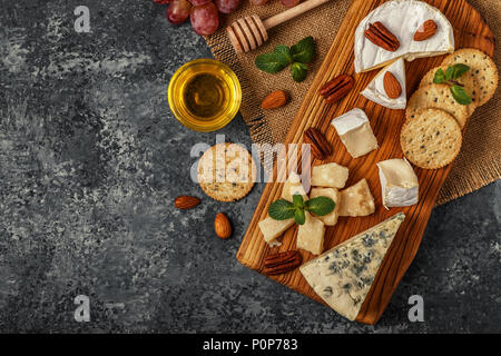 Assortment of cheese with honey, nuts and grape on a cutting board, top view. Stock Photo