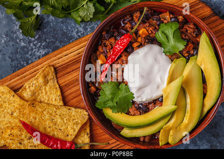 Chili con carne in bowl with avocado and sour cream, top view. Stock Photo
