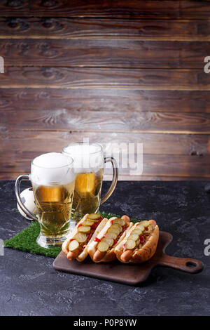 Photo of two mugs of foam beer, green grass with football, hotdogs Stock Photo