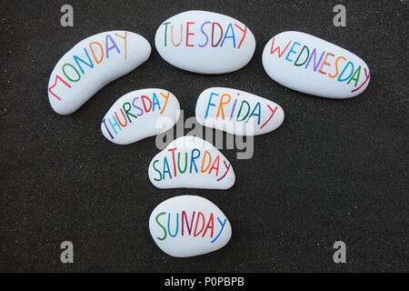 Days of the week carved and painted on sea stones over black volcanic sand Stock Photo