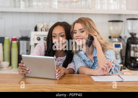 young multiethnic waitresses smiling while looking at digital tablet on bar Stock Photo